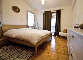 Un dormitorio con una cama de madera, una mesita de noche, una silla, un aparador y una ventana con cortinas.