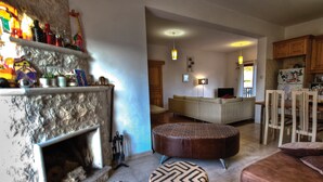 Una sala de estar con chimenea, un sofá, otomanas y un comedor con sillas y una mesa.