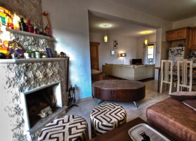 Una sala de estar con chimenea, un sofá, otomanas y un comedor con sillas y una mesa.