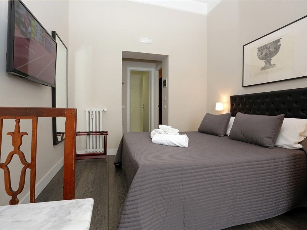 A hotel room with a large bed, a television, a radiator, and a framed artwork on the wall.