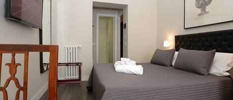 A hotel room with a large bed, a television, a radiator, and a framed artwork on the wall.