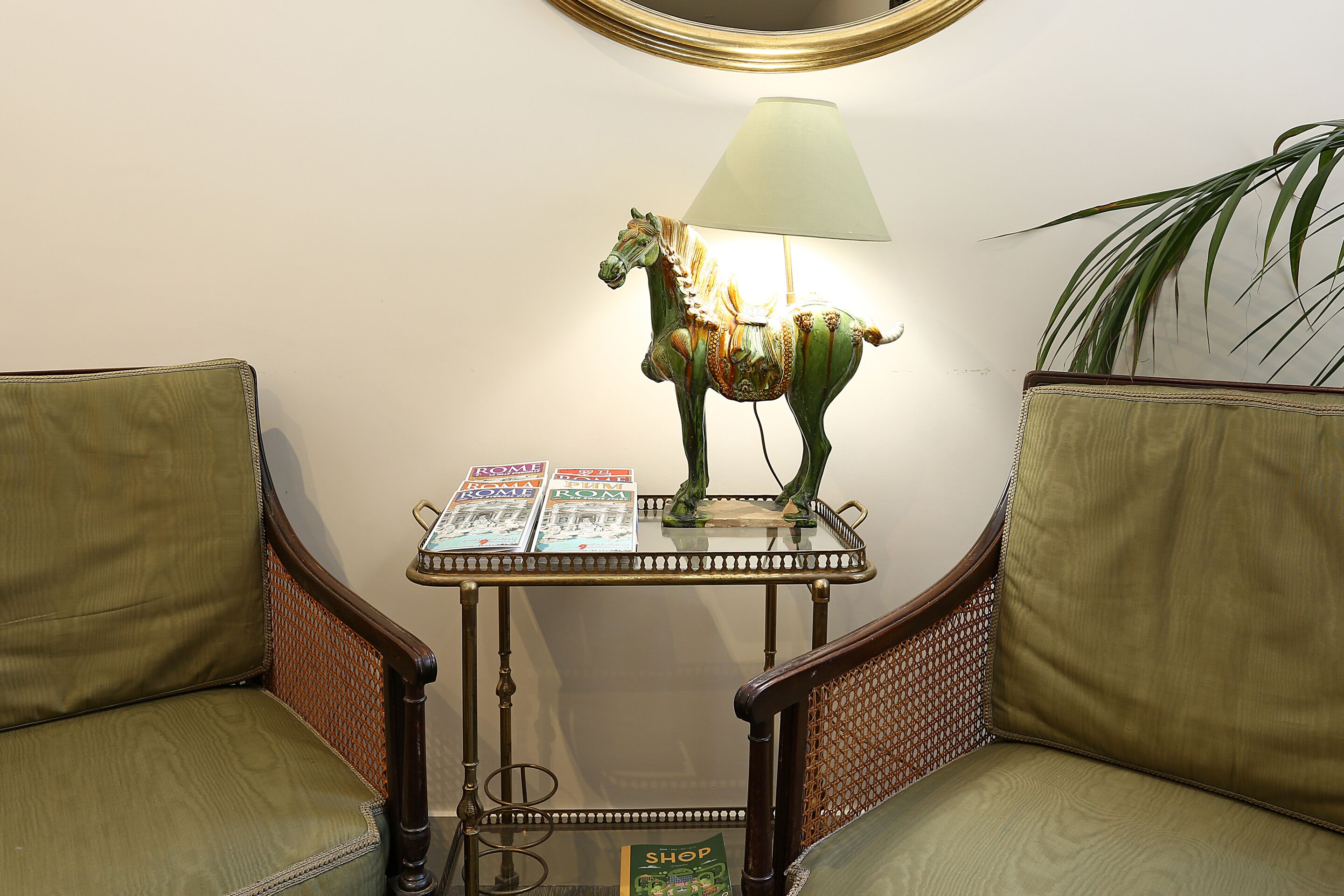 A room with a glass-top table, a lamp, a decorative horse, and two upholstered chairs.