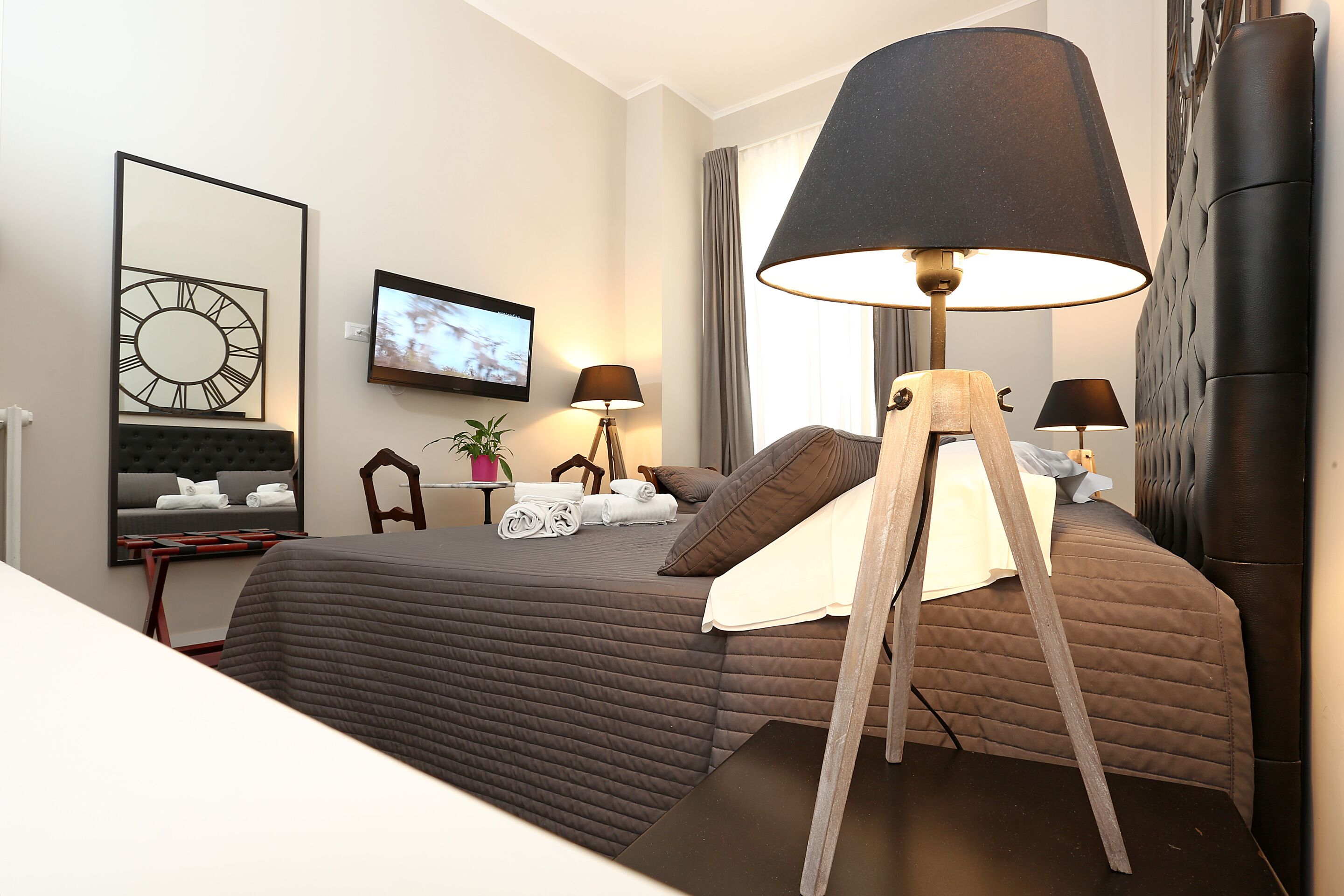 A modern hotel room with a large bed, two bedside tables, a TV, a lamp, and a mirror.
