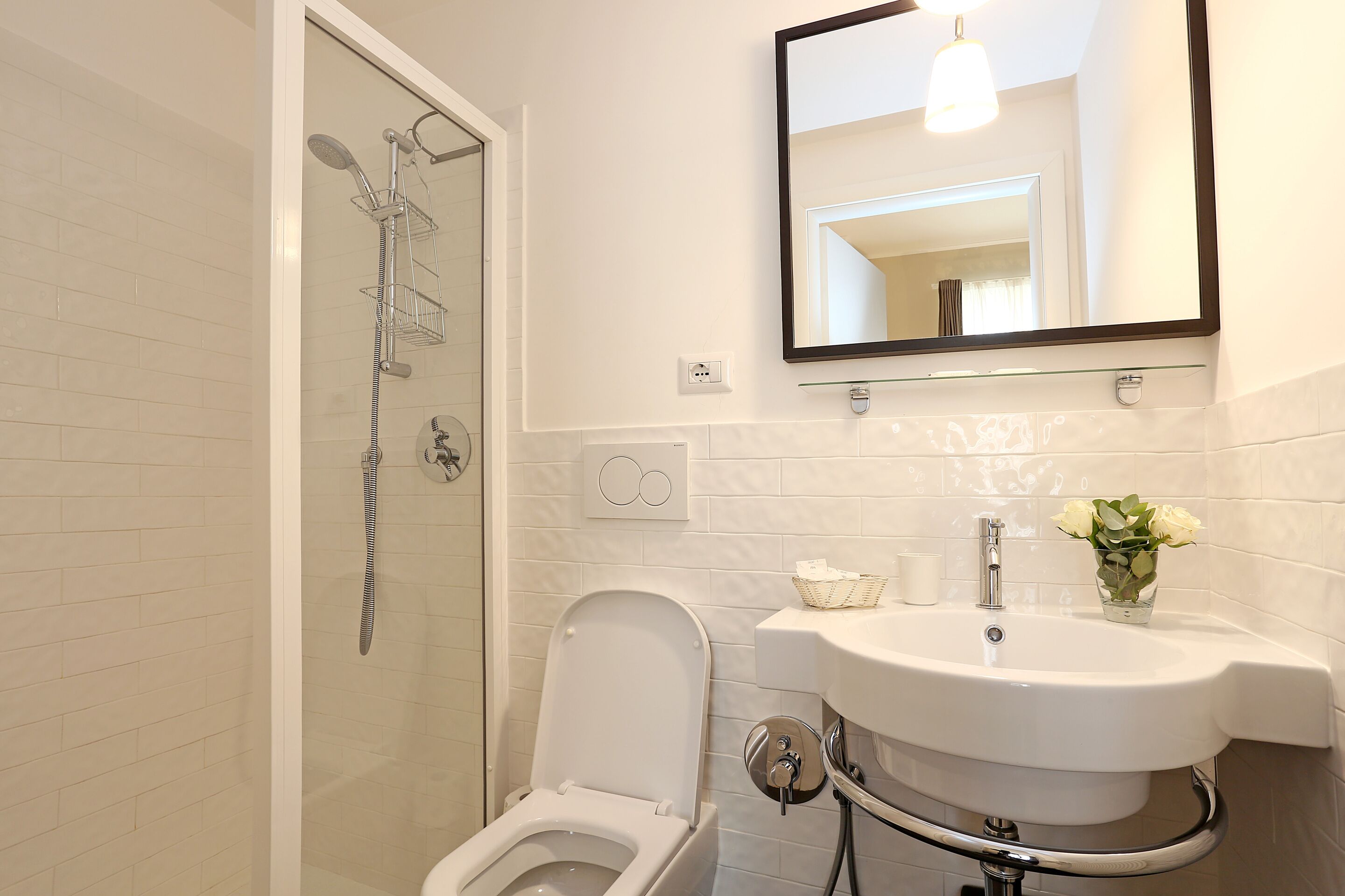 A bathroom with a toilet, sink, shower, and a mirror.