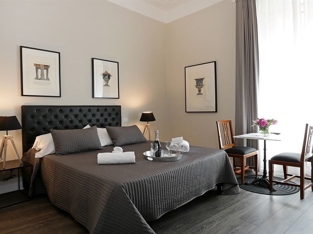 Et hotelværelse med en stor seng, et sengebord, en stol, et lille bord og billedkunst på væggen.