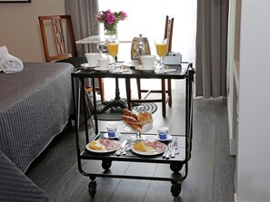A hotel room with a bed, a breakfast trolley with food and drinks, a table with a vase of flowers, and a window with curtains. - Residenza Cavour (Rome)
