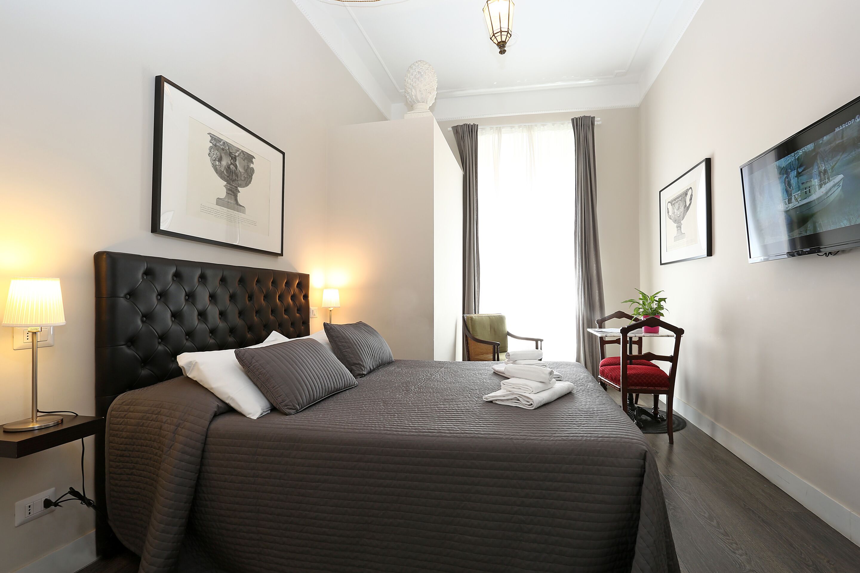 A hotel room with a large bed, a headboard, a flat-screen TV, a framed artwork, and a window with curtains.