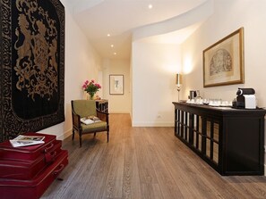 Une chambre d’hôtel avec un plancher en bois, une valise rouge, une chaise verte, une console noire et une grande tapisserie au mur.