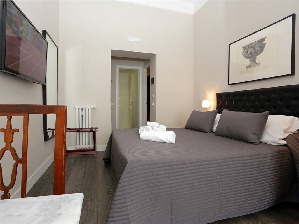 A hotel room with a bed, a radiator, a television, and a framed picture on the wall.