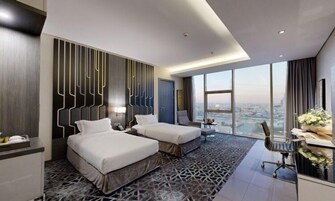 A modern hotel room with two beds, a desk, and a large window offering a city view.