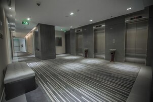 A modern hotel lobby with a striped carpet, a bench, and two elevators.