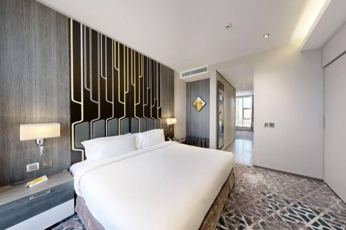 A modern hotel room with a large bed, a decorative wall panel, and a patterned carpet.