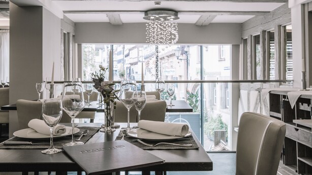 A dining area with tables set for two, featuring wine glasses, plates, and cutlery.
