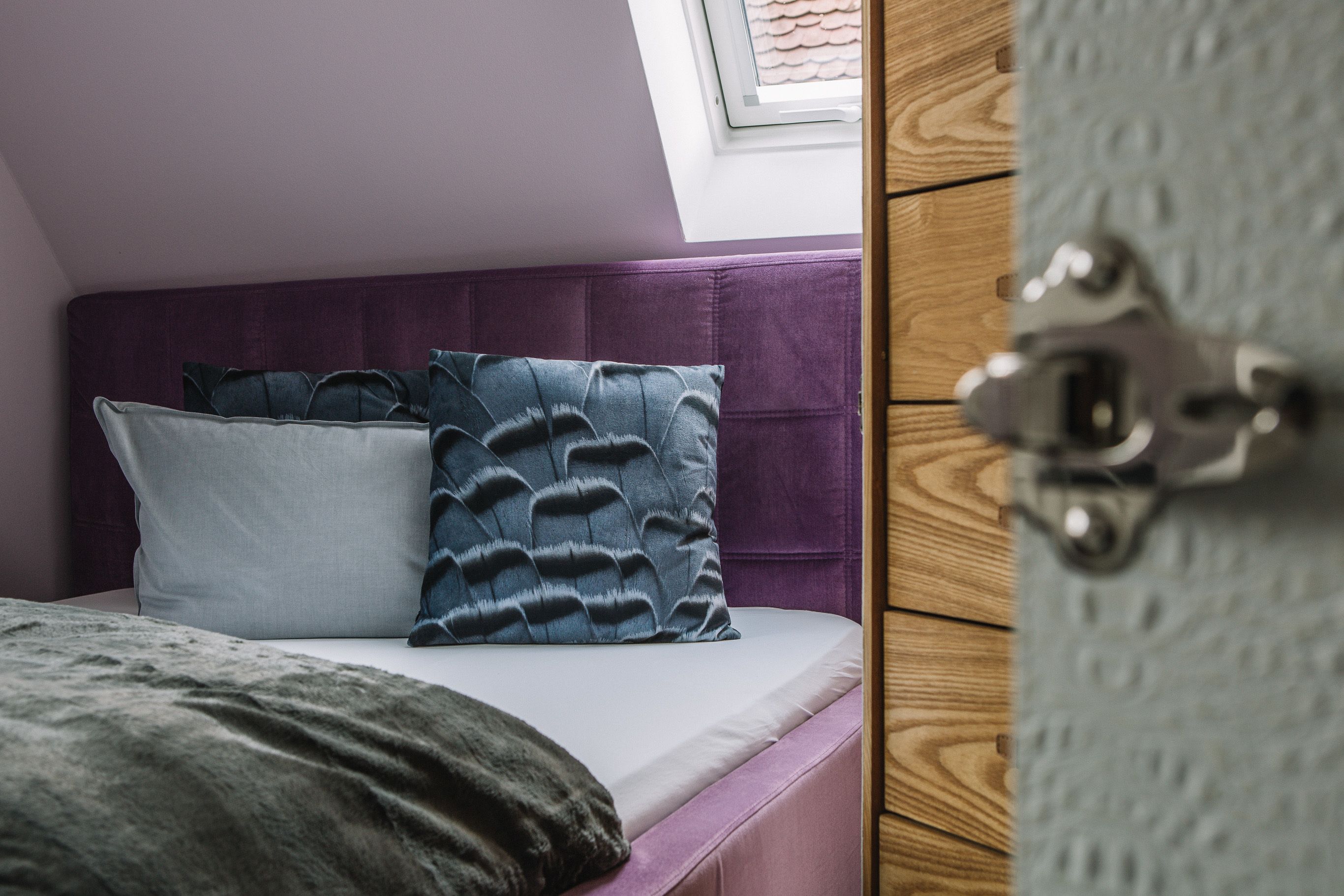 Un dormitorio con cama, cabecero morado y tragaluz.