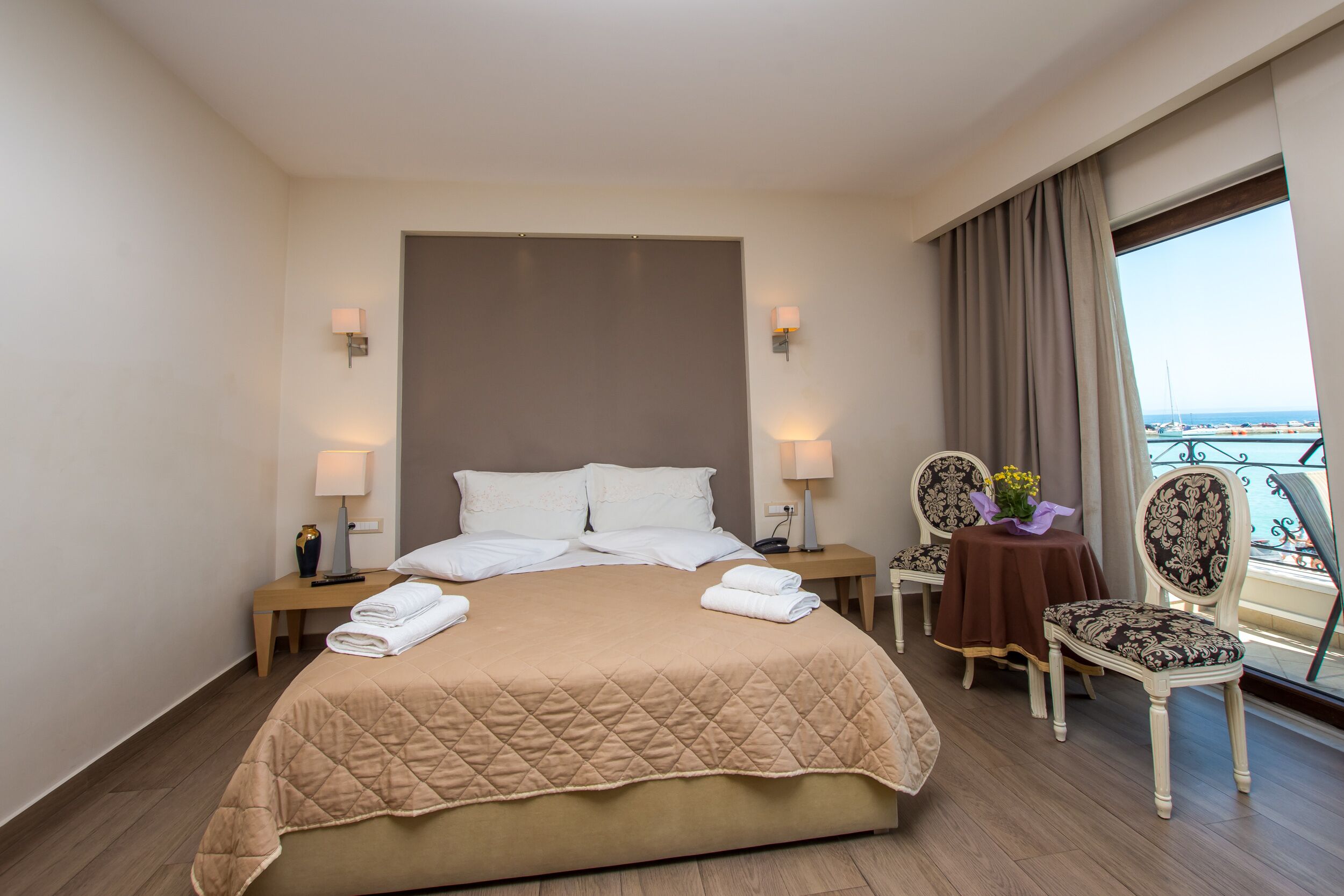 A hotel room with a large bed, two bedside tables with lamps, a chair, and a balcony view.