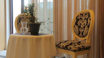 A table with a potted plant and a glass, a chair with a patterned cushion, and a window with curtains.