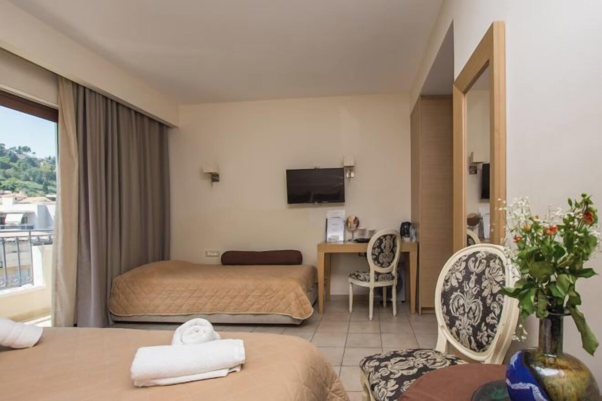 A hotel room with two beds, a desk, a chair, a TV, and a balcony with curtains.
