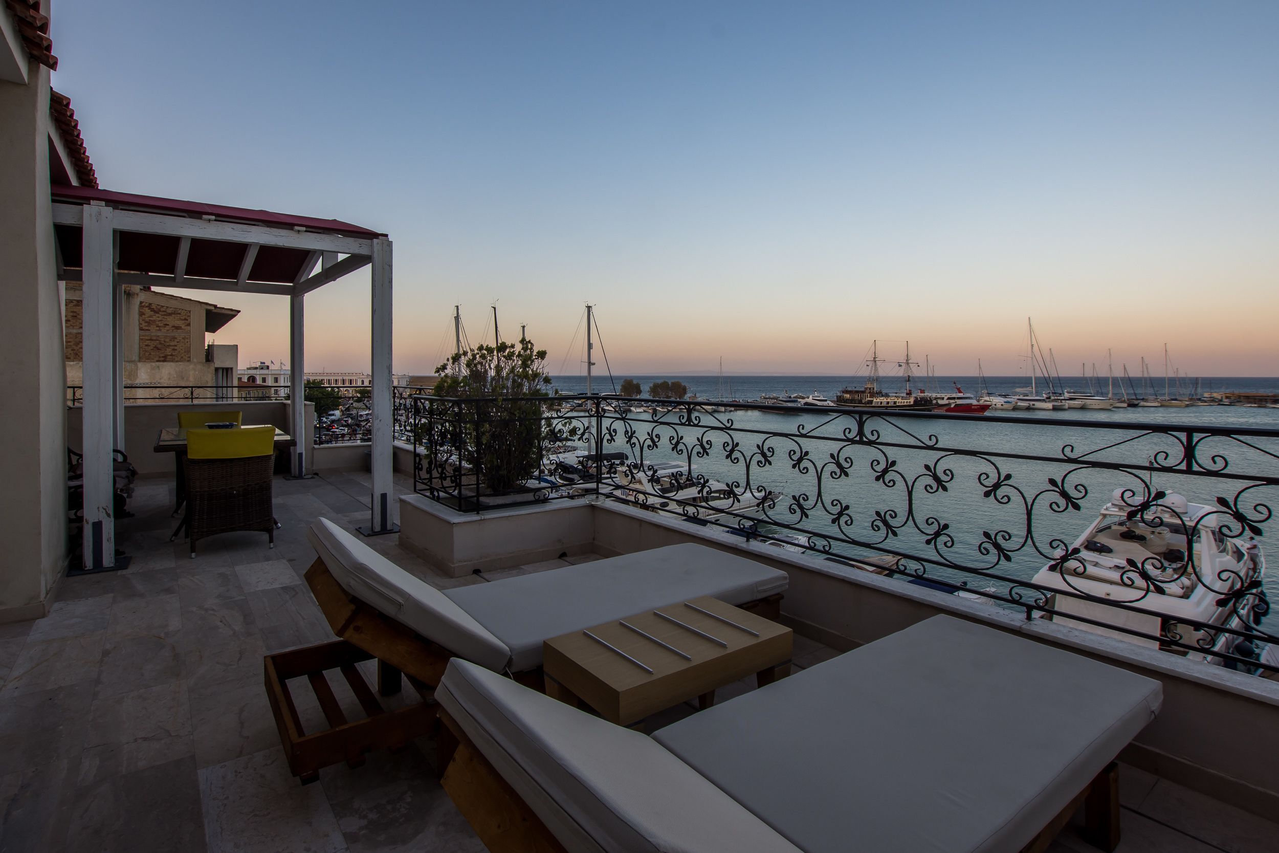 A terrace with lounge chairs and a table, overlooking a marina with boats.