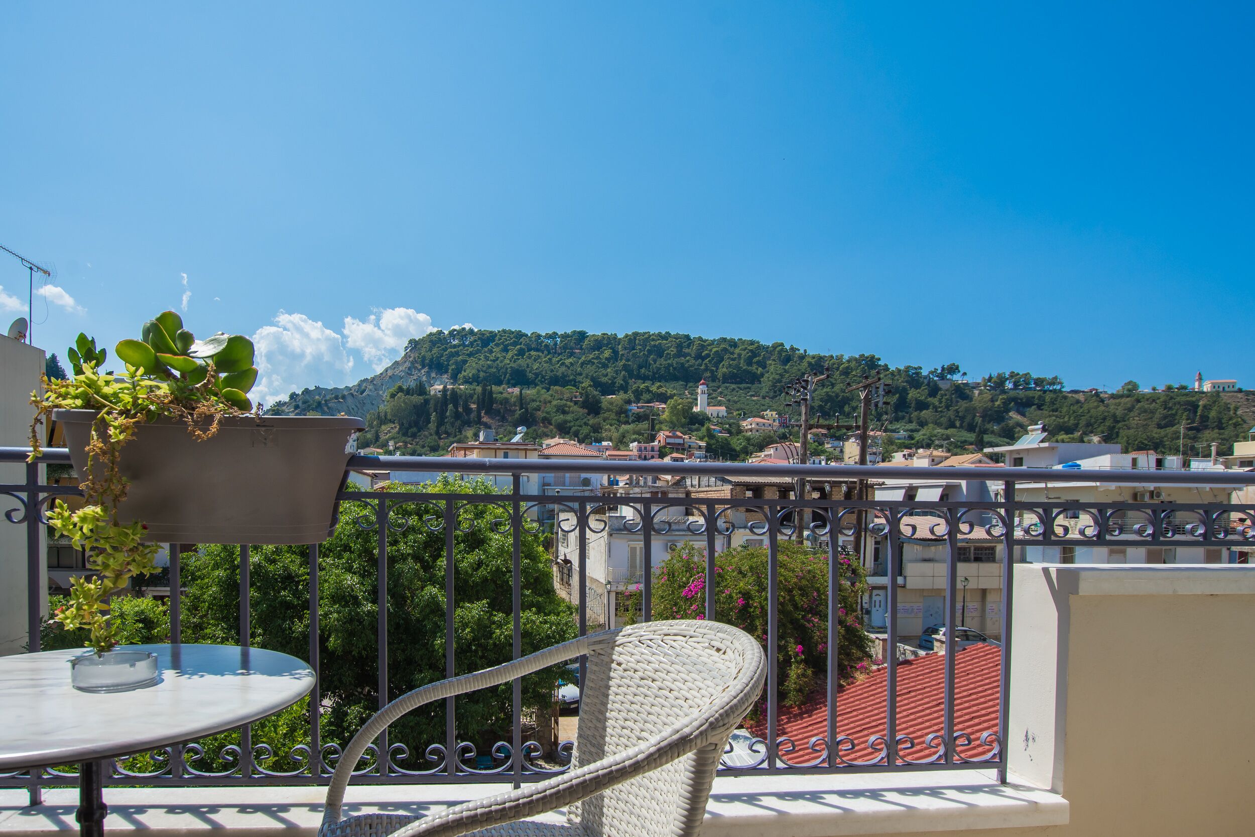 A balcony with a table and chair, overlooking a hillside with buildings and a lighthouse.