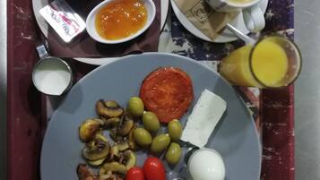 Una bandeja con un plato de comida que incluye huevos, tomates, aceitunas, champiñones y jamón, junto con dos tazas de café y un vaso de jugo.