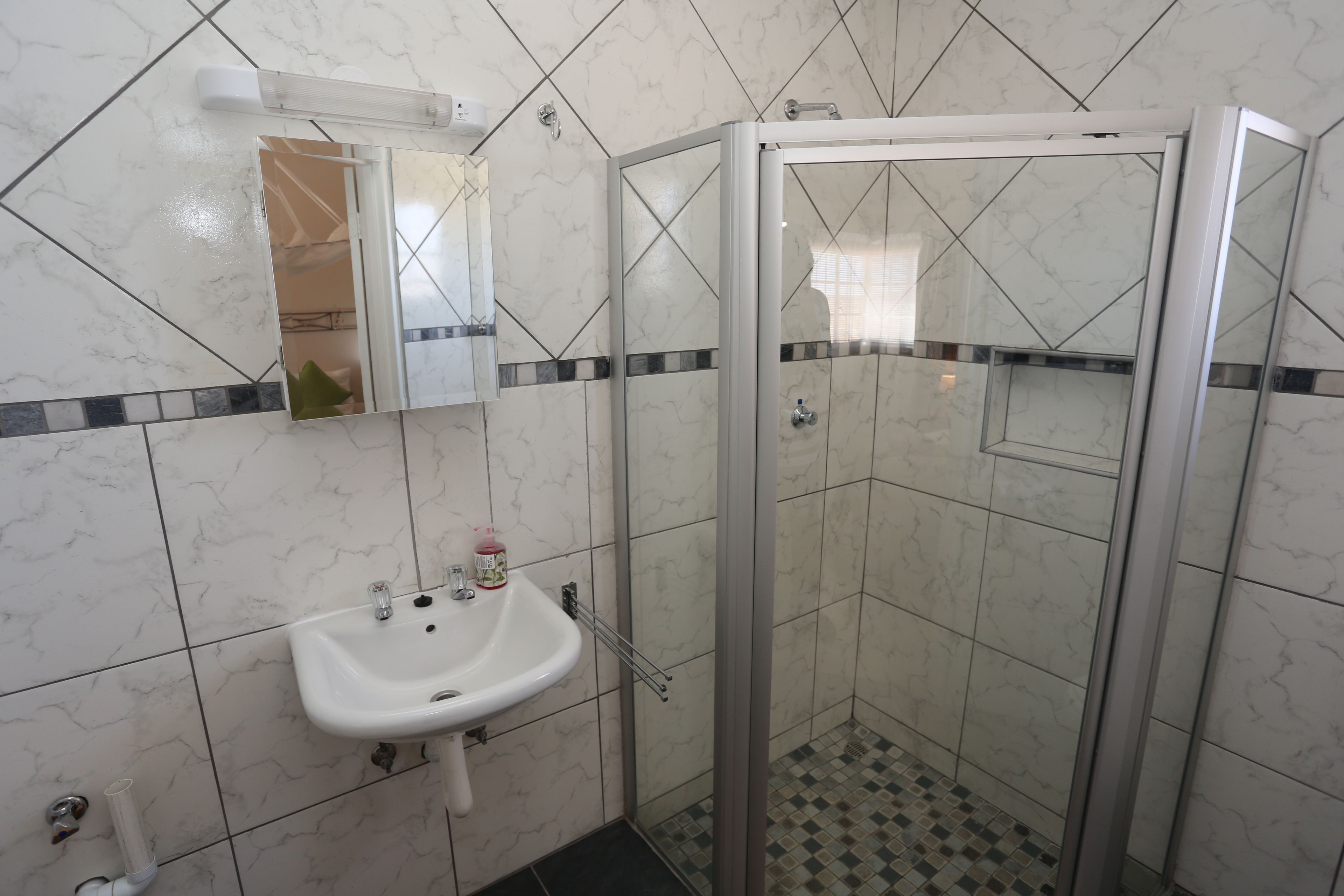 Une salle de bain avec un lavabo blanc, un miroir et une douche à parois de verre.