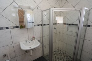 A bathroom with a white sink, a mirror, and a glass-enclosed shower. - Aus Self-Catering Units (Aus)