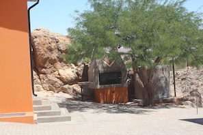 A barbecue area with a stone wall, a tree, and a paved walkway. - Aus Self-Catering Units (Aus)