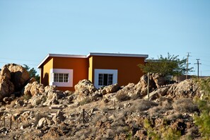 A two-story building with a flat roof, surrounded by rocky terrain and sparse vegetation. - Aus Self-Catering Units (Aus)