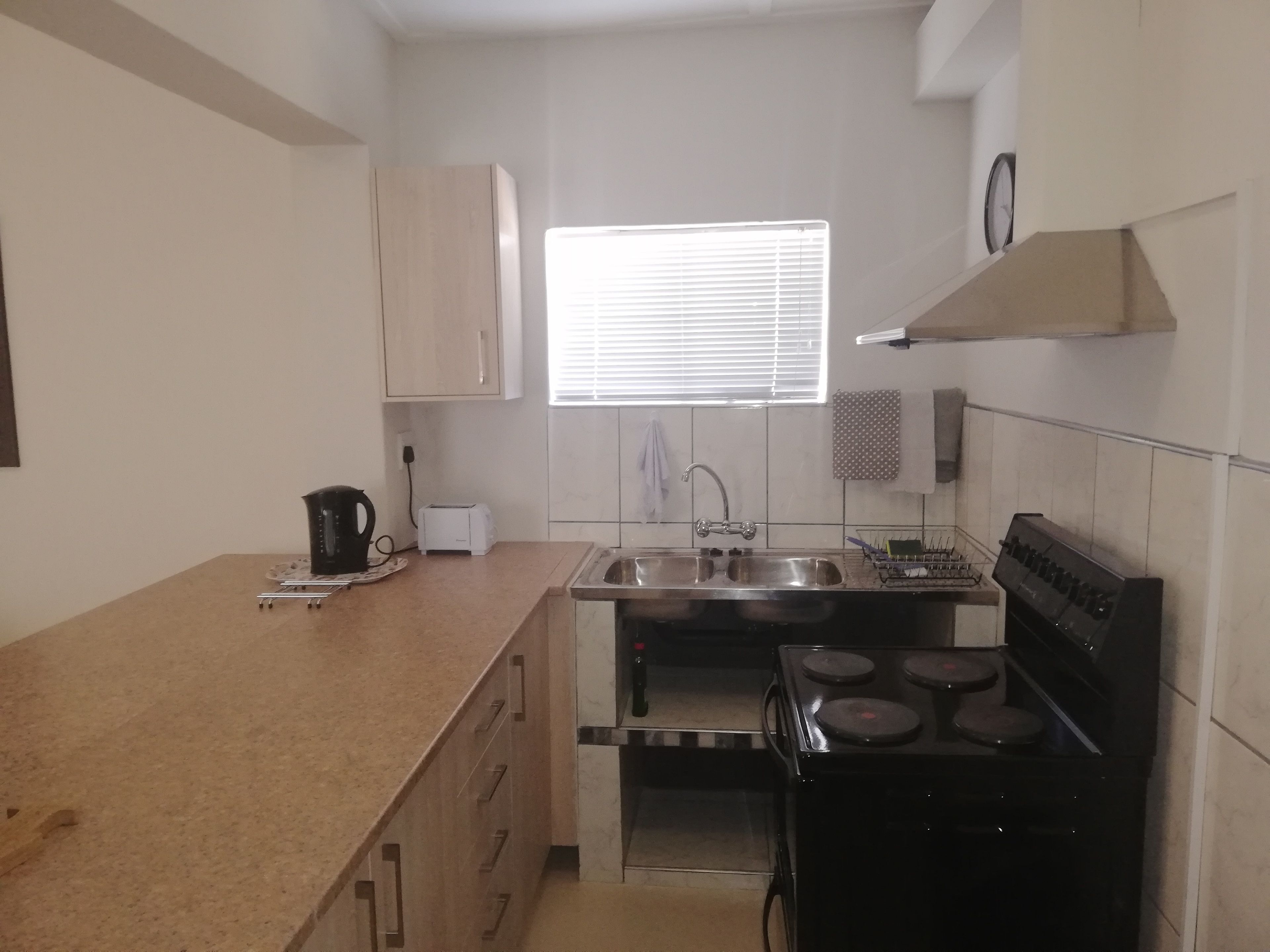 A compact kitchen with a stove, sink, and a window with blinds.