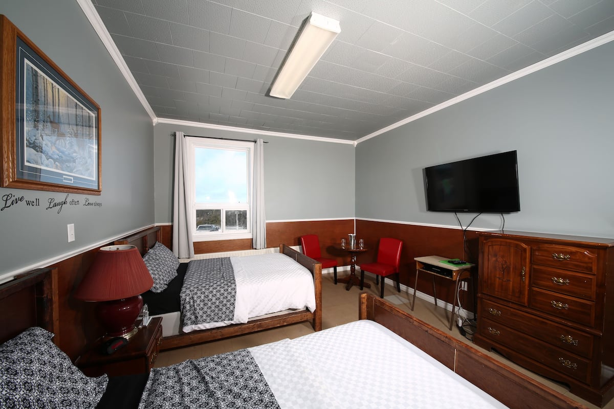 A hotel room with two beds, a wooden dresser, a television, and a window with curtains.