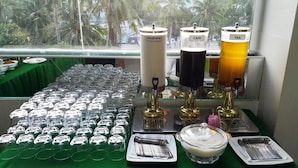 A beverage station with labeled dispensers, a row of glasses, and a bowl of food. - Thi Long Phung Hotel (Phu Quoc)