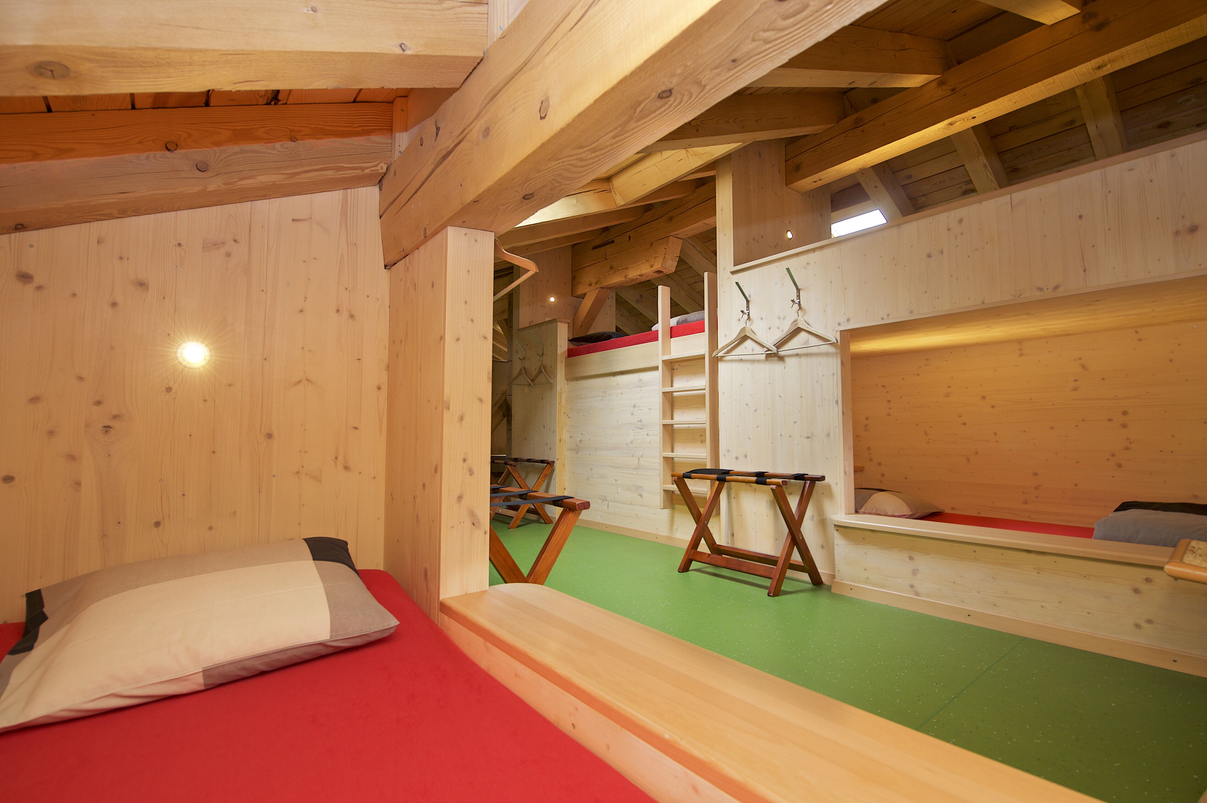 Une pièce en bois avec des lits superposés, une échelle et une moquette verte.