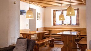 A rustic interior with wooden benches and tables, a high ceiling with exposed beams, and hanging wicker lamps. - Hotel Bahnhof (Zermatt)