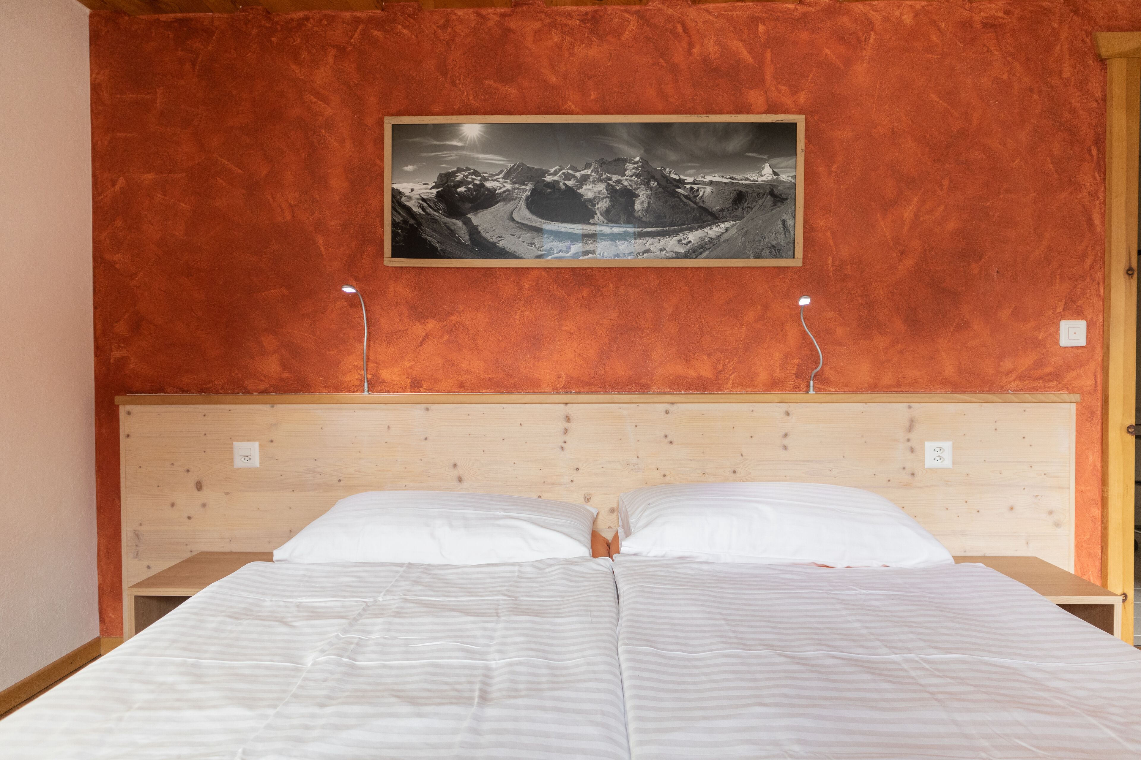 A double bed with white linens in a room with a wooden headboard and a red textured wall.