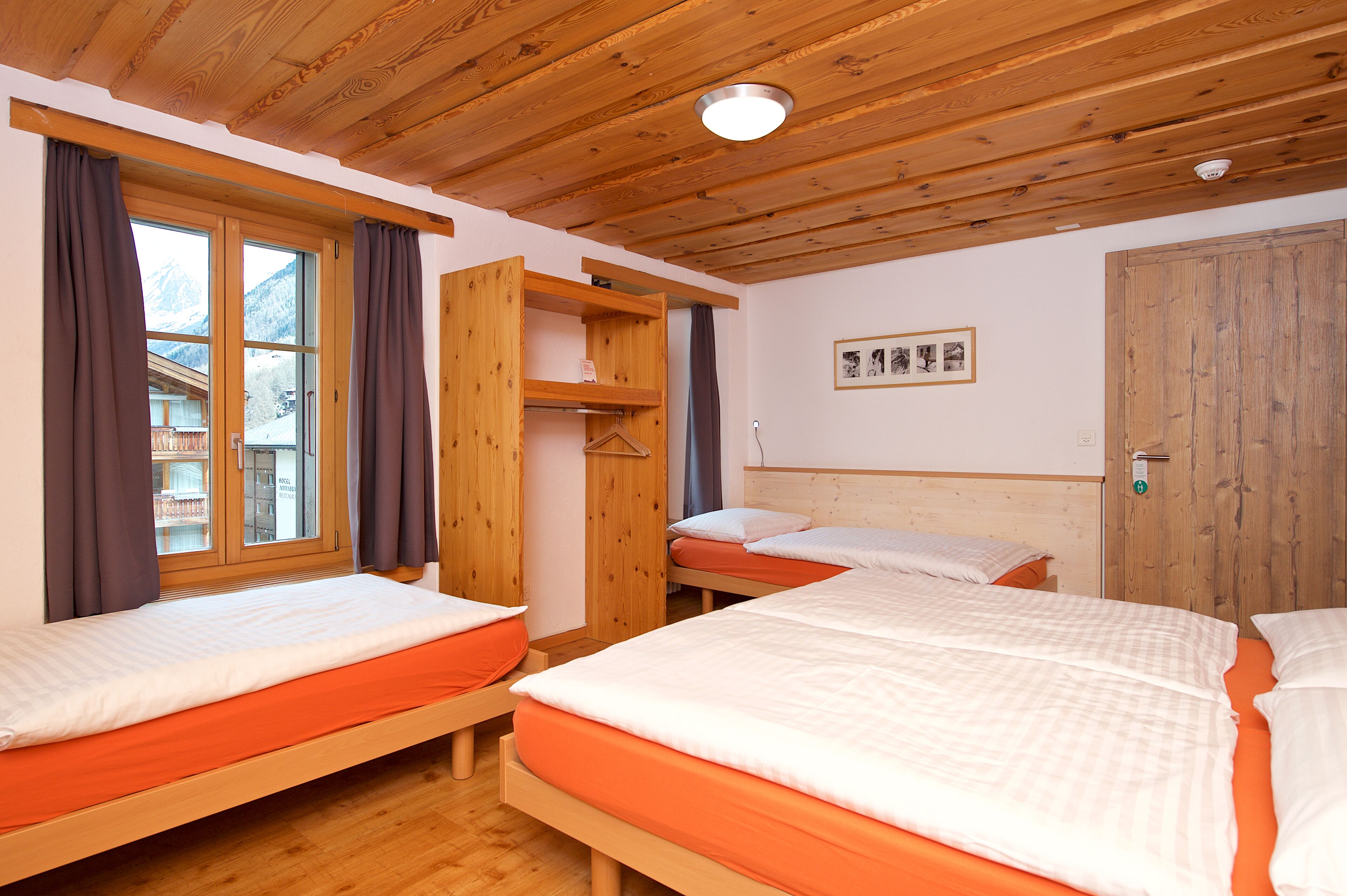 Una habitación con tres camas de madera, un armario de madera y una ventana con cortinas.