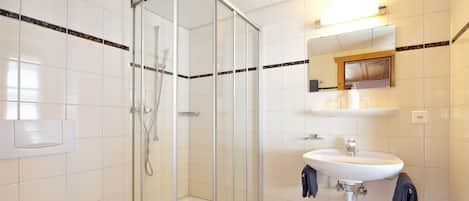 A modern bathroom with a glass-enclosed shower, a white sink with a mirror above, and a towel rack.