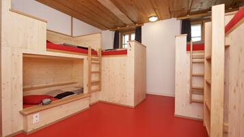 A room with bunk beds, wooden walls, a red floor, and a window with curtains.