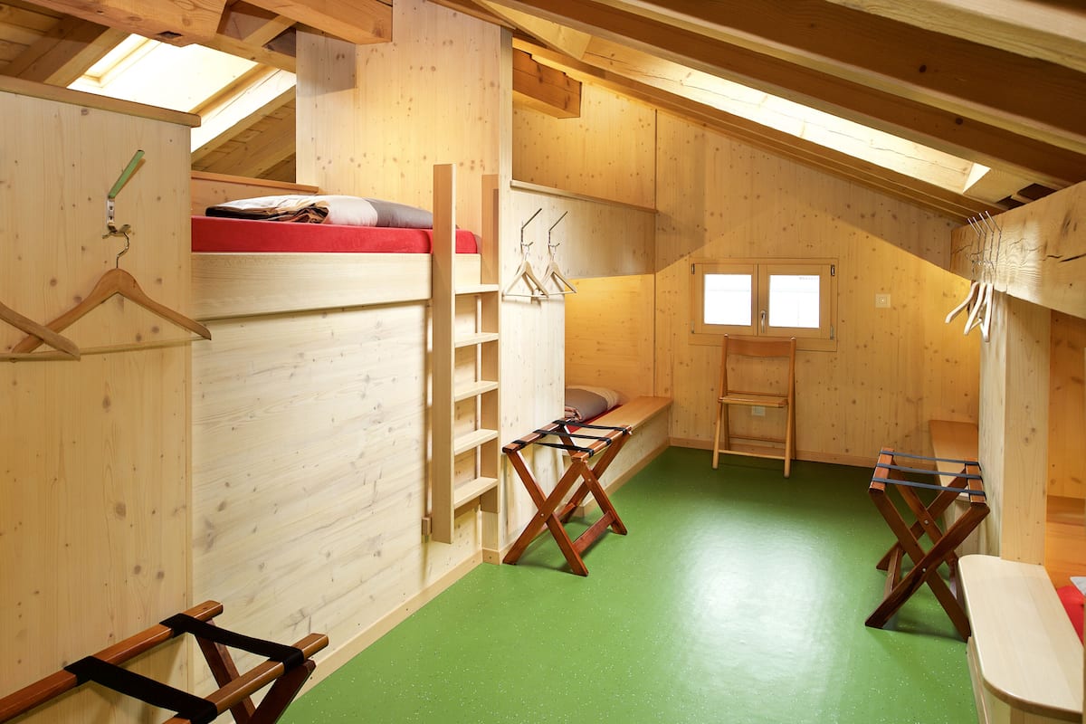 Una habitación de madera con literas, piso verde y una ventana.