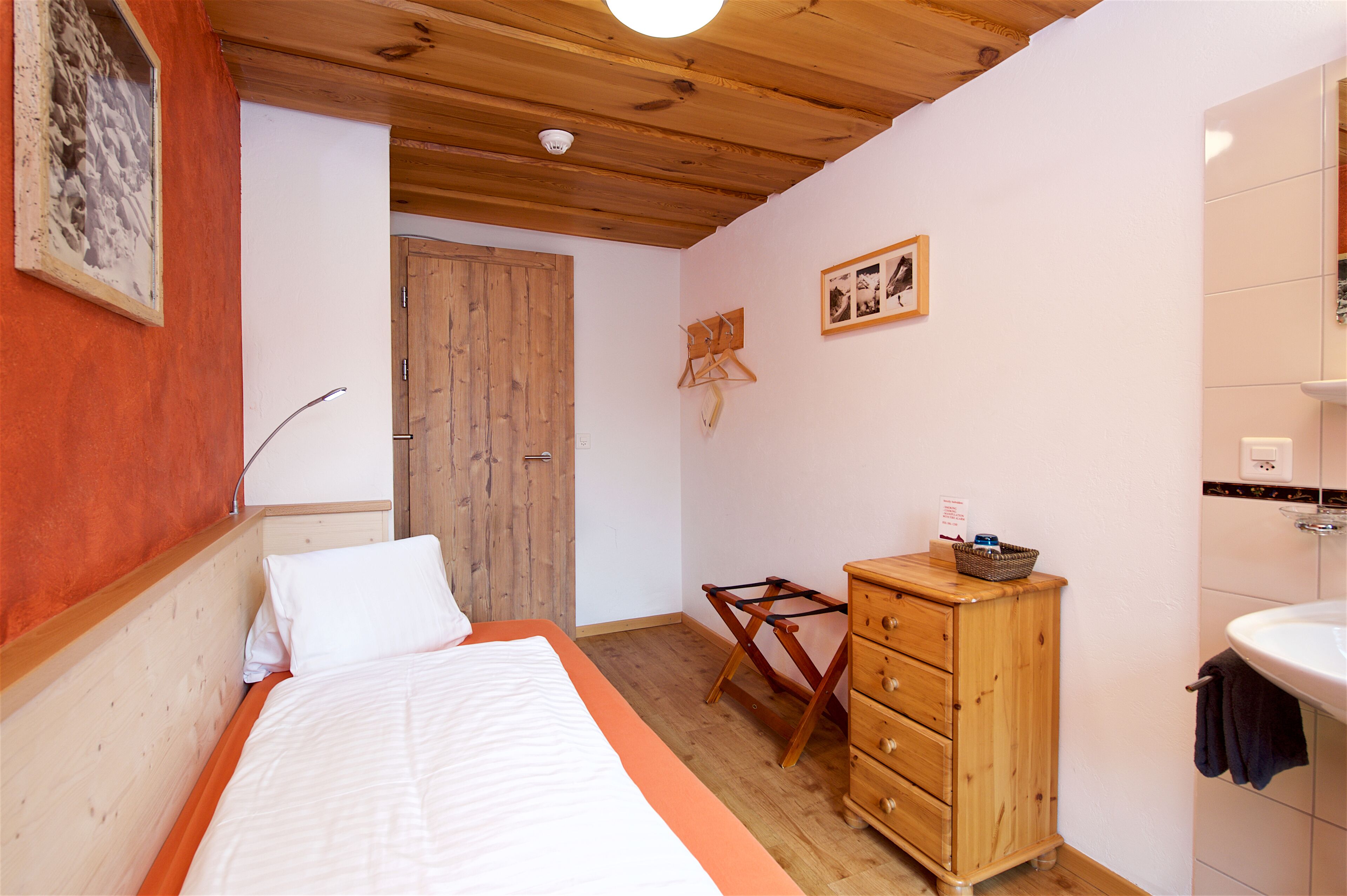 A bedroom with a wooden bed, a wooden dresser, a wooden wardrobe, and a bathroom with a sink and mirror.