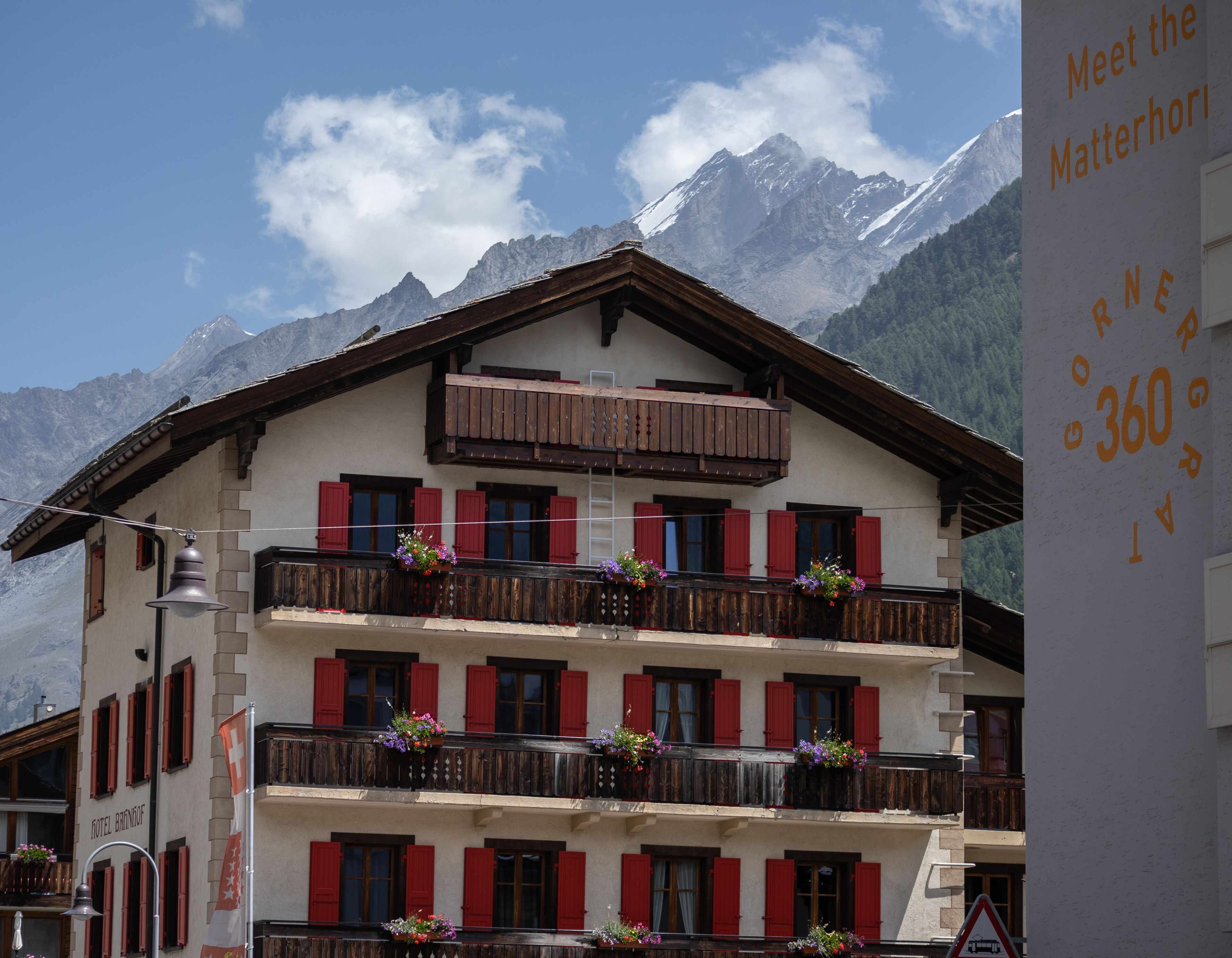 Ein mehrgeschossiges Hotel mit Balkonen, die mit Blumenkästen geschmückt sind, vor der Kulisse schneebedeckter Berge.