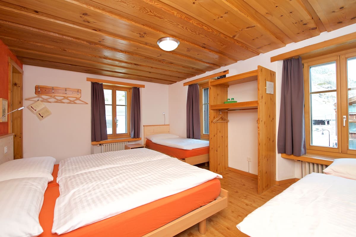 Una habitación con paneles de madera, dos camas, un estante de madera y una ventana con cortinas.