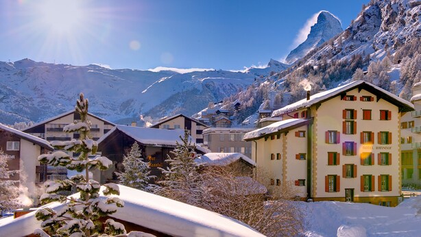 A hotel with multiple buildings, snow-covered surroundings, and mountains in the background. - Hotel Bahnhof (Zermatt)