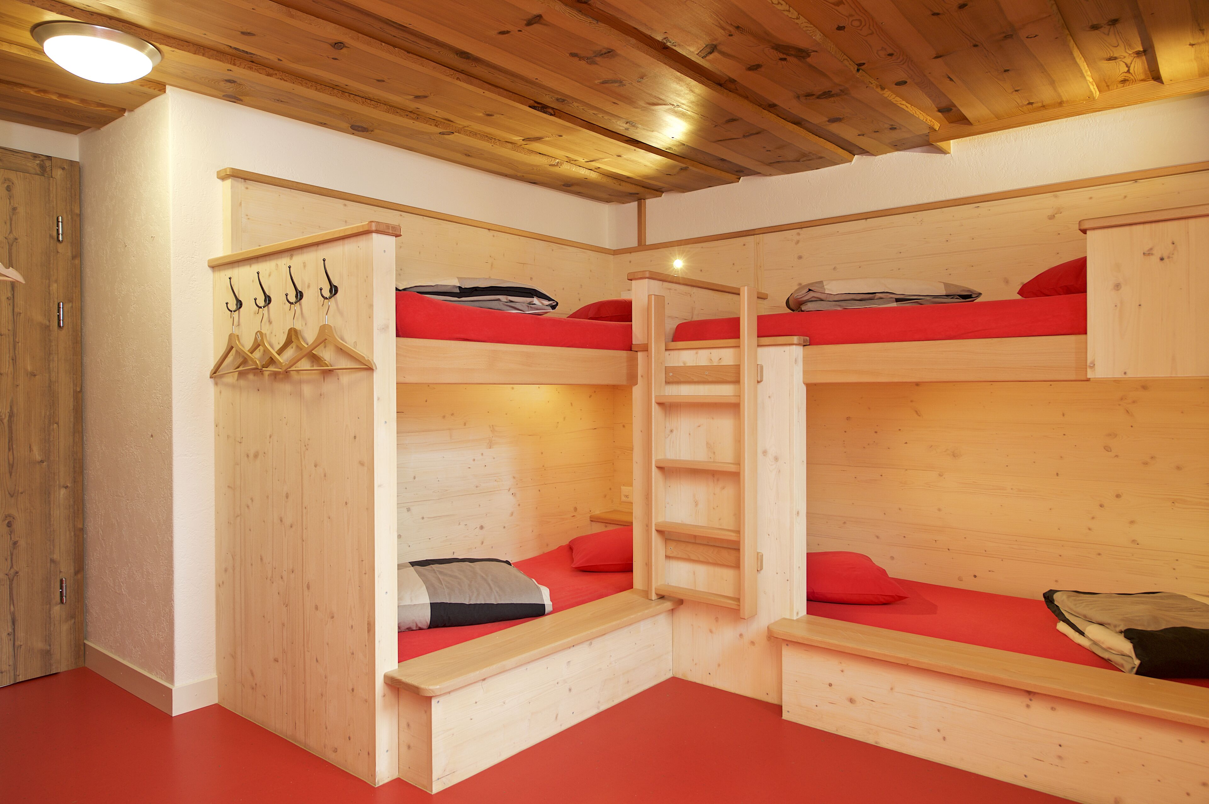 Habitación con literas de madera, alfombra roja, paredes de madera y techo con vigas a la vista.