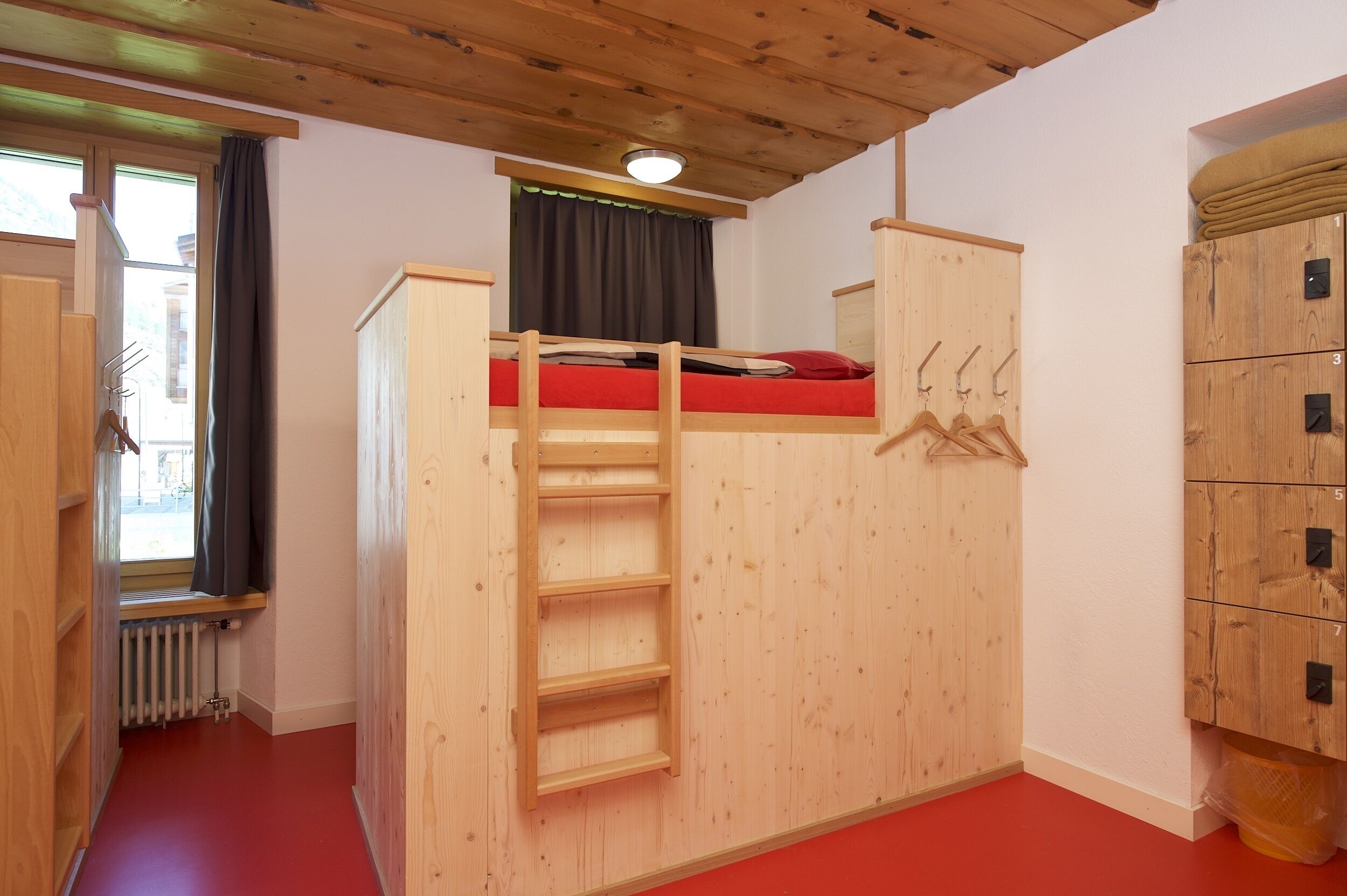Una cama litera con escalera, una ventana con cortinas y un armario de madera.