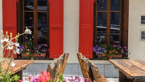 A building with red shutters and flower boxes on the windows. There are wooden benches in front. - Hotel Bahnhof (Zermatt)