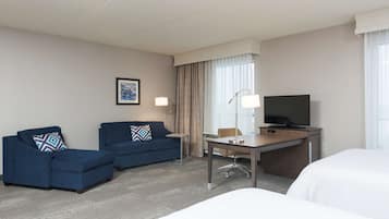 Quarto de hotel com cama, escrivaninha, poltrona, sofá e televisão.