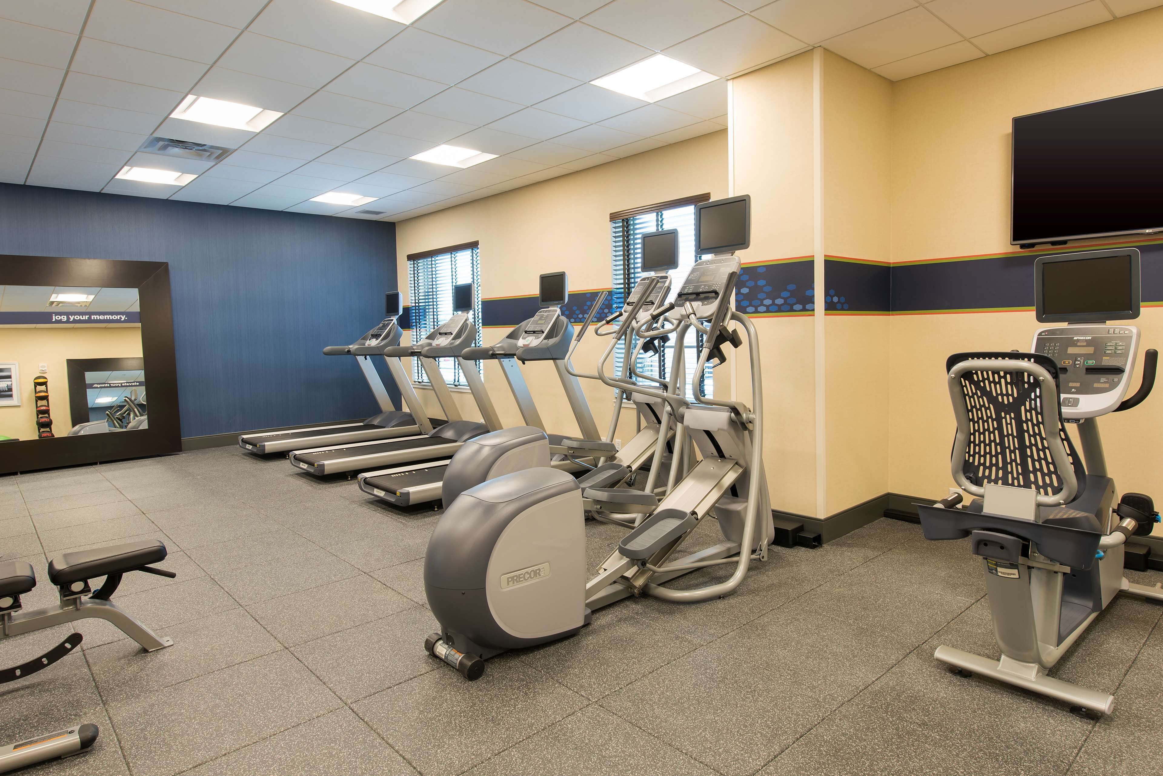 Une salle de sport équipée de tapis de course, de vélos elliptiques et d’un banc de musculation.
