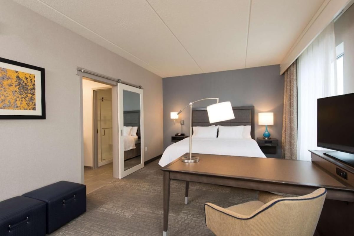 A hotel room with a bed, bedside tables, a desk, a chair, a television, and a door leading to a bathroom.
