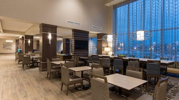 Un amplio vestíbulo de hotel con varias zonas de estar, un ventanal con vistas y luminarias modernas.