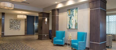 A lobby with two blue armchairs, a patterned rug, and a large abstract painting on the wall.